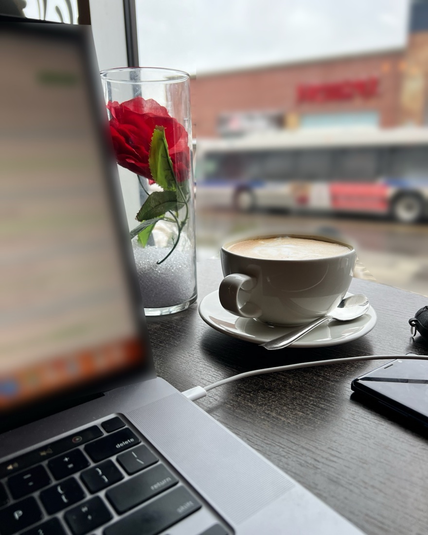 A laptop, a coffee and a rainy street view from a café table